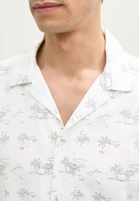 Korte mouwenshirt van witte linnen met een palmboomprint, met een camp collar, knoopsluiting en subtiele pastelaccenten.
