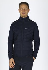 Marineblå zip-up jakke med polstret front, glatte ærmer, reflekterende detaljer og sidelommer for funktionalitet. Letvægts og tætsiddende design.