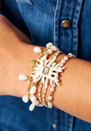 Weißes und goldenes Perlenarmband mit einem Seestern-Anhänger, Perlenakzenten und kleinen Muscheldetails, präsentiert an einem Handgelenk.
