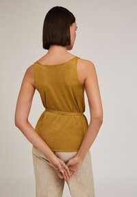 Top senza maniche in oro metallico con vestibilità rilassata. Presenta una vita con cintura e una superficie liscia. Visto da dietro, mette in risalto il colletto.