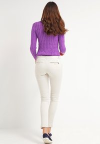 Lila kabelstickad tröja, åtsittande vita byxor och blå skor. Outfiten har ett texturerat garn och en smal silhuett. Bakifrån visad.