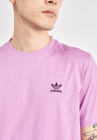 Lila pamut póló kerek nyakkal és rövid ujjal, bal mellen kis fekete Adidas logóval. Sima textúra.