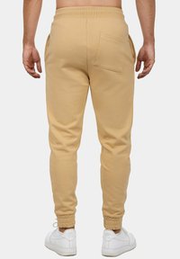 Beige joggerbroeken met een taps toelopende pasvorm, een elastische tailleband, een achterzak en ribgebreide boorden. G gedragen met witte sneakers.