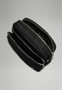Černá nylonová taška se dvěma přihrádkami, vybavená kovovými zipy a síťovinovými akcenty. Hladký povrch a minimalistický design.