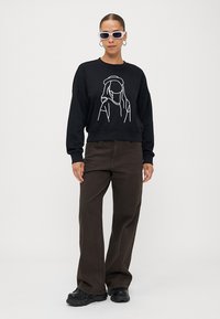 Sweatshirt preto com design em arte de linha branca na frente, combinado com calças largas castanhas escuras e ténis chunky pretos.