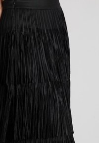 Gonna a frange nera a strati indossata con un top nero, che mostra la texture dettagliata e il movimento del tessuto.