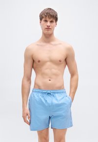 Ανοιχτό μπλε μαγιό με κορδόνι στη μέση, πλαϊνές τσέπες και λεία υφή. Διαθέτει λογότυπο της μάρκας κοντά στο τελείωμα στην αριστερή πλευρά.