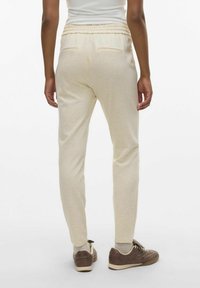 Lichtbeige sweatpants met een geribde tailleband, twee achterzakken en taps toelopende pijpen. De stof is zacht en licht gebroken.
