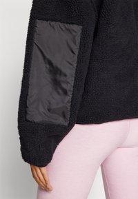 Sort fleece-pullover med en tekstureret overflade og en blank sort stoflap på ærmet. Har en afslappet pasform og blød tekstur.