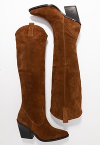 Braune Overknee-Stiefel aus Wildleder mit spitzer Zehenpartie, Blockabsatz und Ziernähten, ausgestattet mit einem Zuglaschen an der Rückseite für einfaches An- und Ausziehen.