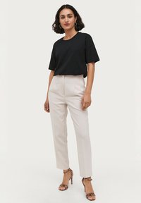 Sort bomuld t-shirt, afslappet pasform, sammen med højtaljede, lysebeige bukser. Accenteret med mønstrede, remverse hæle.