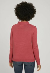 Long-sleeve sweater in bright pink knit, featuring a high neck, ribbed texture, and a relaxed fit. Clean hem at the waist.