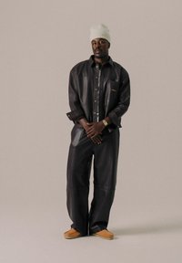 Sort læder oversized jakke med brystlomme, knaplukning foran og bredbenede sorte læderbukser. Tan slip-on sko fuldender looket.