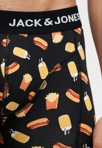 Κοντινή λήψη μαύρων μποξεράκι Jack & Jones με σχεδιασμούς από χοτ ντογκ, πατάτες τηγανιτές και κίτρινα ποτά με καλαμάκια.