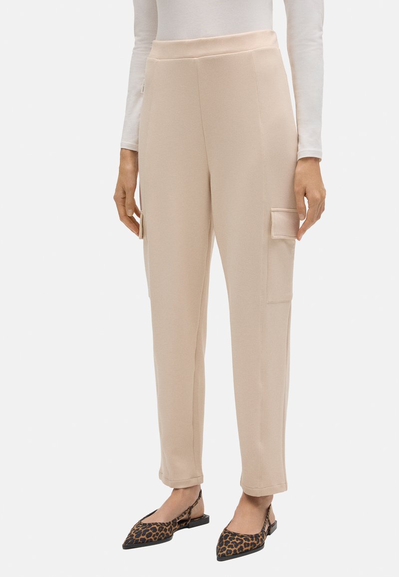 Pantalones cargo beiges con una cintura alta, bolsillos laterales y un diseño de pierna ajustada, confeccionados en una tela suave y elástica.
