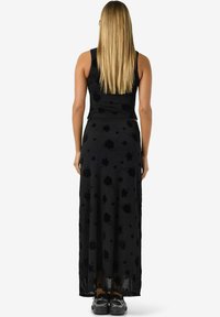 Svart blomstrete maxikjole med tettsittende overdel, gjennomsiktig skjørt og teksturerte blomster. Kombinert med svarte sneakers og langt rett hår.