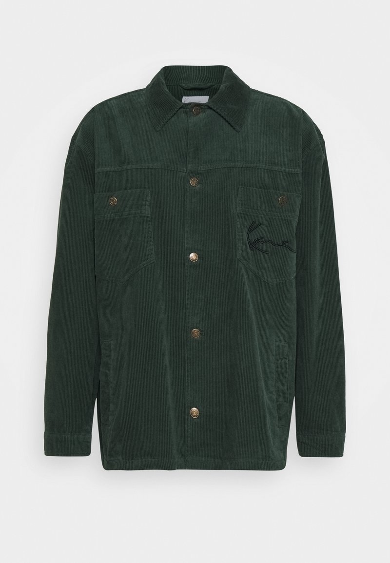 Grön manchesterjacka med krage, framknappar, två bröstfickor och en broderad logotyp på vänster sida. Strukturerad tyg.