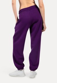 Lila Jogginghosen mit einem gerippten Bund und elastischen Bündchen. Weicher Stoff mit lockerer Passform, kombiniert mit weißen Sneakern.