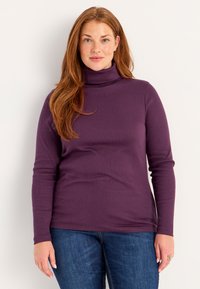 Purple turtleneck top, long sleeves, soft fabric with a smooth texture, paired with blue jeans, featuring a fitted silhouette.