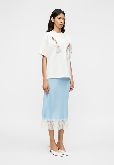 Λευκό T-shirt με δαντελωτά  παπούτσια τοποθετημένα στο μπροστινό μέρος; φούστα από ανοιχτό μπλε σατέν με λευκή δαντέλα στο τελείωμα; μυτερά λευκά τακούνια. Μινιμαλιστικός σχεδιασμός.