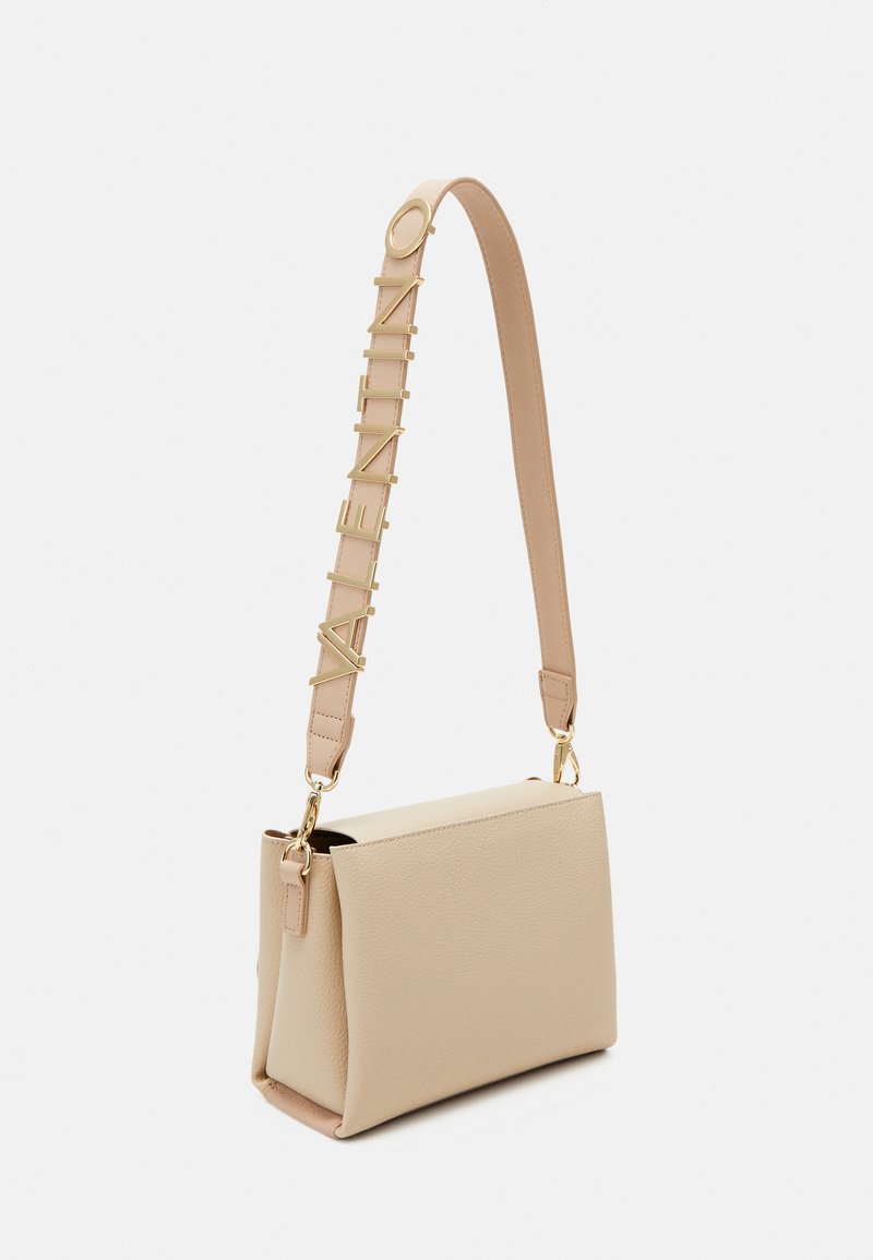 Sac en cuir beige avec une forme structurée, présentant une finition texturée et une bandoulière ornée de lettres dorées épelant "VALENTINO."