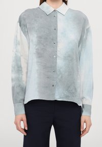 Camicia button-up leggera in tie-dye pastello con colletto a punta, maniche lunghe e una sottile trama, dotata di diversi bottoni sul davanti.