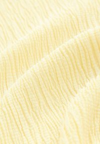 Tissu texturé d'un jaune doux, présentant un motif froissé avec des rayures en relief, créant de la profondeur et un intérêt visuel.