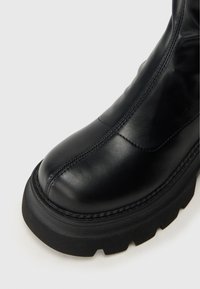 Čierne kožené členkové topánky s zaoblenou špičkou, pevným gumovým podošvom a výraznými švovými detailmi na vrchnej časti.