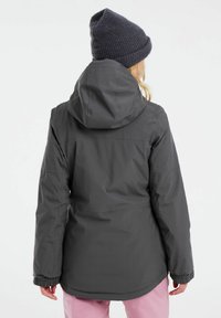 Graue wasserdichte Jacke mit Kapuze, elastischen Bündchen und geradem Schnitt. Über rosa Hosen getragen, die ein praktisches Design haben.