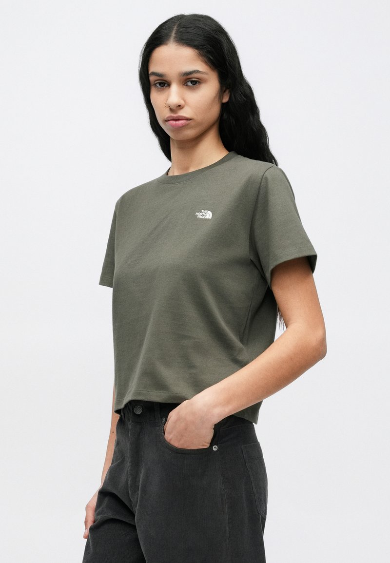 Olive green short-sleeve cotton t-shirt with a round neckline and small white logo on the chest, styled with dark pants.