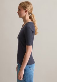 Marineblauw geribbelde top met korte mouwen en een V-hals, gecombineerd met lichtblauwe denim jeans. De gladde textuur en aansluitende pasvorm benadrukken de silhouette.