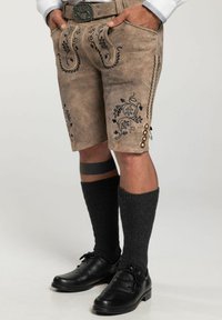 Braune Lederhosen mit kunstvoller blauer Blumenstickerei, ausgestattet mit Seitentaschen und Knöpfen, kombiniert mit schwarzen knielangen Socken und Schuhen.