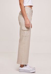 Beige cargo bukser med en afslappet pasform, med en sidelomme, bæltestropper og lige snit; parret med hvide sneakers.