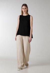 Zwarte mouwloze top met een geplooid ontwerp, gecombineerd met lichtbeige brede broek met verticale strepen en een relaxte pasvorm.