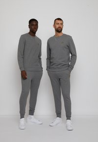 Sweatshirts et joggings gris en tissu doux, avec un petit logo jaune sur la poitrine, associés à des baskets blanches.