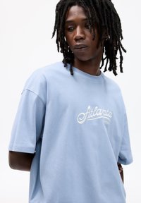 Light blue cotton t-shirt with short sleeves, featuring white embroidered "Atlanta Georgia" text on the front. Casual fit and smooth texture.