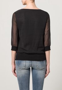 Svart genomskinlig blus med trekvartslånga ärmar, smockad midja och en avslappnad passform. Texturerad tyg ger en lätt utseende.