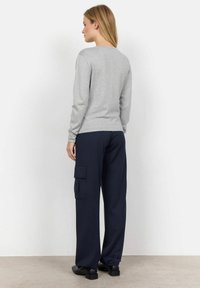 Maglietta grigia a maniche lunghe con scollo rotondo, abbinata a pantaloni cargo larghi blu navy con tasche laterali e vestibilità comoda. Scarpe nere.