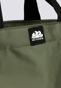 Borsa a mano in tessuto verde con manici neri. Presenta un grande patch del logo SUNDEK in nero. Il design è semplice e funzionale, realizzato in materiale testurizzato.