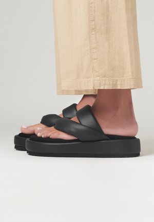 Černé platformové sandály mají silnou podrážku a design se zkříženými pásky z hladké kůže. Stélka je tvarovaná pro pohodlí.