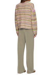Multikleurige gebreide trui met horizontale strepen in pastelkleuren, met een relaxte pasvorm. Gecombineerd met lichtgrijze wijde broek.