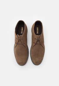 Brown suede shoes with a low profile, featuring a rounded toe, two eyelet lace design, and a textured sole. Geox branding visible inside.