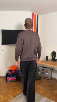 Sweatshirt marron avec poignets côtelés, associé à un pantalon noir à jambes larges. L'intérieur présente un mur d'accent coloré et divers objets décoratifs.