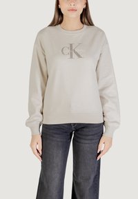 Sudadera beige con mangas largas, dobladillo y puños acanalados. Presenta un logotipo bordado central con "Calvin Klein" en una fuente sutil.