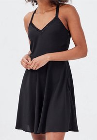 Black sleeveless dress with a V-neckline, featuring lace detailing on straps and a loose, A-line shape. Smooth fabric with a subtle texture.