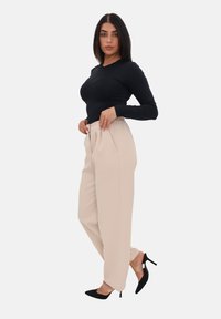Maglia nera a maniche lunghe abbinata a pantaloni beige a vita alta con elastico in vita e tasche frontali, completata da scarpe con tacco nere.