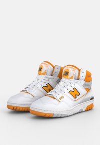 Białe skórzane sneakersy do koszykówki z pomarańczowymi akcentami. Oferują wysoki krój, wyściełany kołnierz, wyraźne logo 'N' oraz teksturowaną podeszwę.