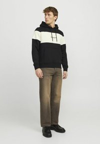 Sort og creme stribet hoodie med frontlomme, snoretræk og broderet logo, parret med brune jeans og sorte sko.