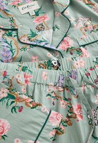 Világoszöld, virágos pizsamaszett rózsaszín virágokkal, rajzfilm állatmintákkal, sötétzöld paszpóllal, gombos gallérral és zsinóros, rugalmas derékkal.