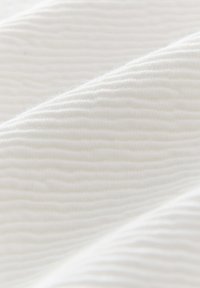 Tissu blanc texturé avec des motifs ondulés subtils, présentant des lignes douces légèrement côtelées et une apparence lisse et légère.